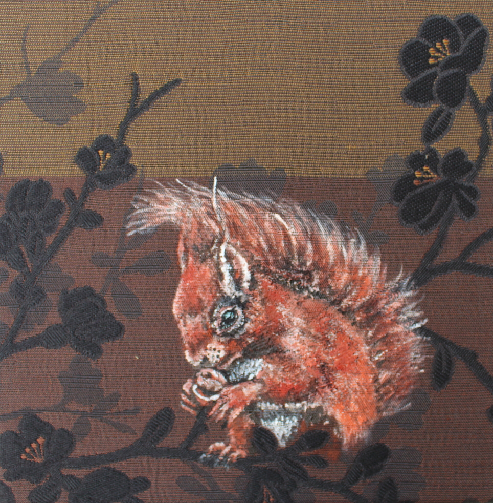 Stoffbild klein: Ein Eichhörnchen knabbert an einer Haselnuss. Der Stoff ist gelb braun mit schwarzen Blüten und Astmuster.